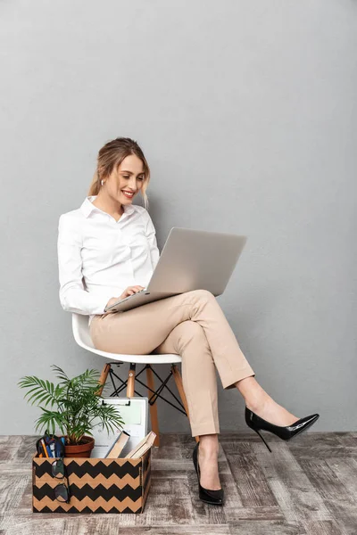 Üzerinde gri duvar arka plan oturma bitki ve dizüstü bilgisayar kullanarak belgeleri kutusu yakınındaki izole kadın. — Stok fotoğraf