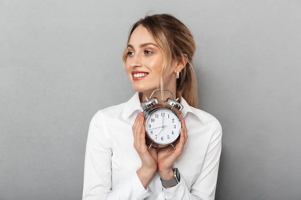 Gelukkig zakenvrouw geïsoleerd over grijs muur achtergrond houden wekker. — Stockfoto