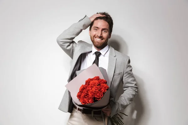 Empresario en ropa formal aislado sobre fondo blanco de la pared sosteniendo flores . — Foto de Stock