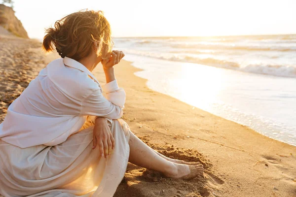 Зображення елегантної жінки 20s сидить на піску і дивиться на море, w — стокове фото