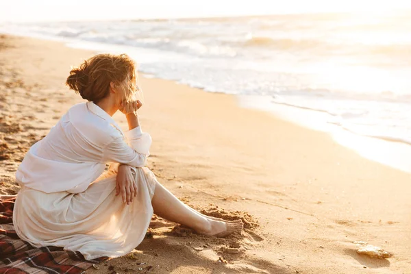 Immagine di una splendida donna 20s seduta sulla sabbia e guardando il mare , — Foto Stock