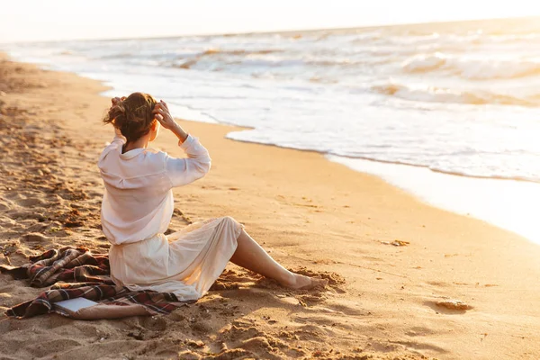 Immagine di una bella donna 20s seduta sulla sabbia e guardando il mare, wh — Foto Stock