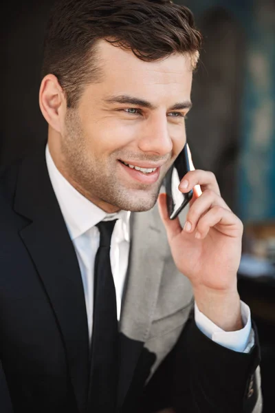 Happy young businessman sitting in cafe talking by mobile phone. — Stock Photo, Image