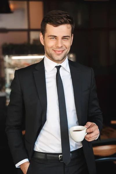 Bonito jovem empresário em roupas formais dentro de casa no café bebendo café . — Fotografia de Stock