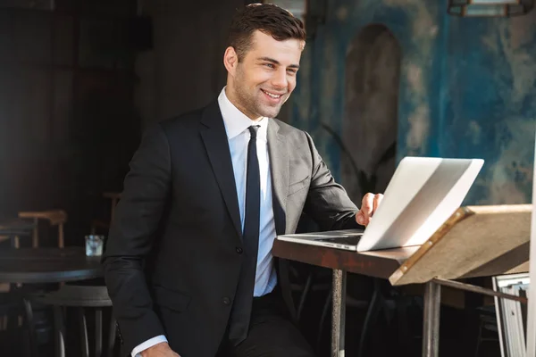 Heureux jeune homme d'affaires assis dans un café à l'aide d'un ordinateur portable . — Photo