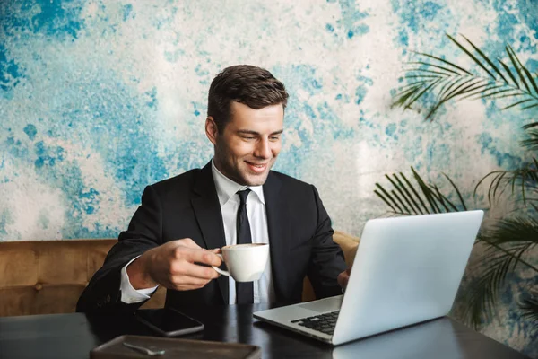 Happy young businessman sitting in cafe using laptop computer. — Stock Photo, Image
