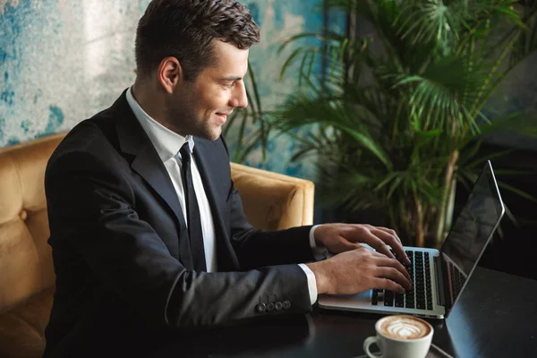 Heureux jeune homme d'affaires assis dans un café à l'aide d'un ordinateur portable . — Photo