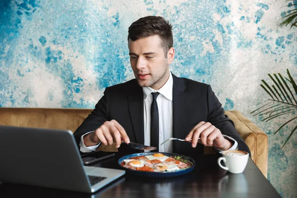 Mladý podnikatel, posezení v kavárně pomocí přenosného počítače mají snídaně nebo večeře jíst. — Stock fotografie