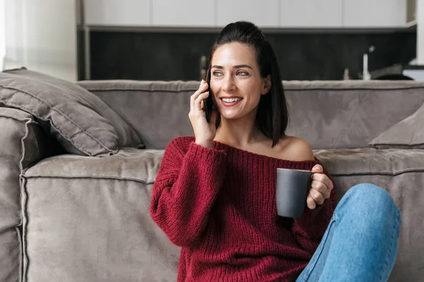 Frau im Haus telefoniert mit dem Handy und trinkt Kaffee. — Stockfoto