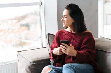 Cep telefonu kullaranarak kanepe kapalı evinde güzel kadın.