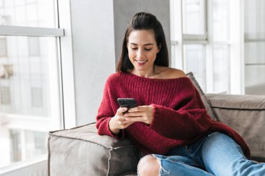 Cep telefonu kullaranarak kanepe kapalı evinde güzel kadın.