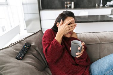 Korkmuş duygusal kadın kapalı kahve kapsayan gözleri içme Tv kanepe üzerinde ev izle.