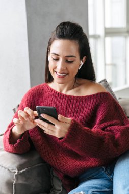 Kadın kapalı kulaklık ile müzik dinleme cep telefonu kullanarak Divan evinde.