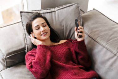 Kadın kapalı eve kanepe kulaklık ile müzik dinleme.