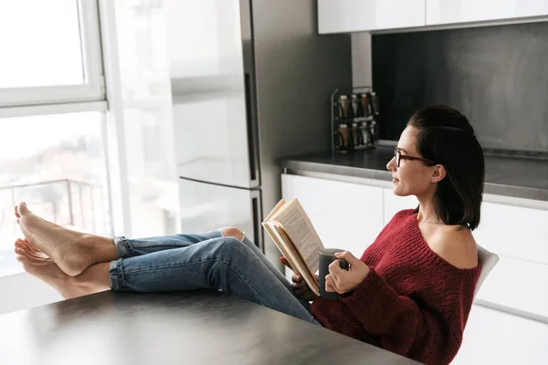 Pretty woman indoors in home at the kitchen reading book. — Stock Photo, Image