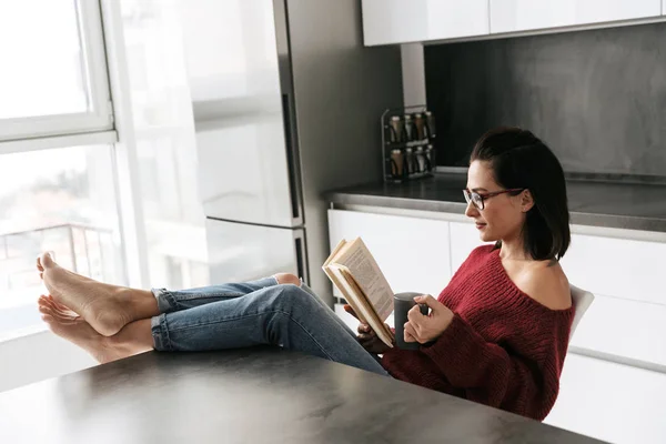 Pretty woman indoors in home at the kitchen reading book. — Stock Photo, Image