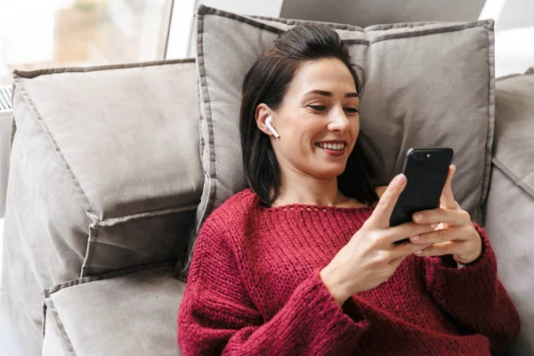 Schöne Frau drinnen im Haus auf dem Sofa mit dem Handy. — Stockfoto