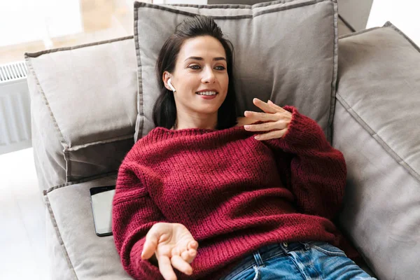 Mujer en casa en el sofá escuchando música con auriculares . — Foto de Stock