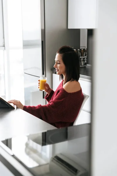 Increíble mujer en el interior de la casa en la cocina usando la tableta de la computadora bebiendo jugo . —  Fotos de Stock