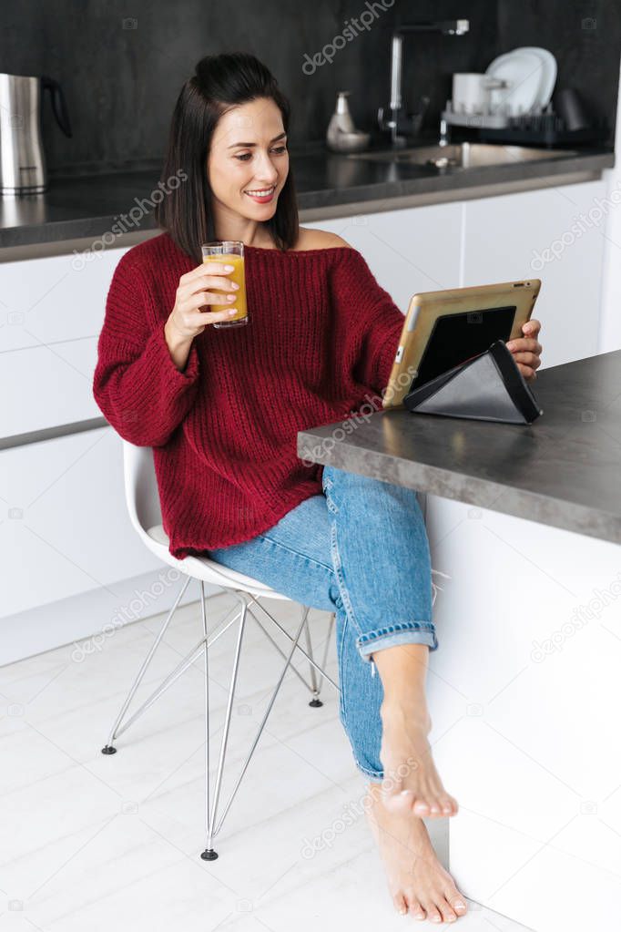 Amazing woman indoors in home at the kitchen using tablet computer drinking juice.