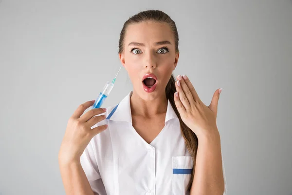 Bonita jovem cosmetologista médico isolado sobre fundo de parede cinza segurando seringa para injetáveis . — Fotografia de Stock