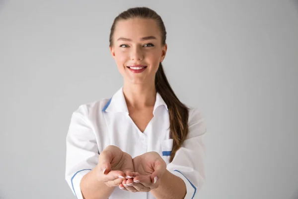 Mooie jonge vrouw schoonheidsspecialist arts geïsoleerd over grijs muur achtergrond weergegeven: een handen. — Stockfoto