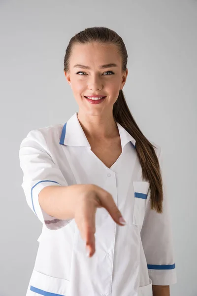 Mooie jonge vrouw schoonheidsspecialist arts geïsoleerd over grijs muur achtergrond geven u een hand voor handdruk. — Stockfoto