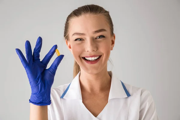 Schöne junge Frau Kosmetikerin Arzt isoliert über graue Wand Hintergrund hält Pille Vitamin. — Stockfoto