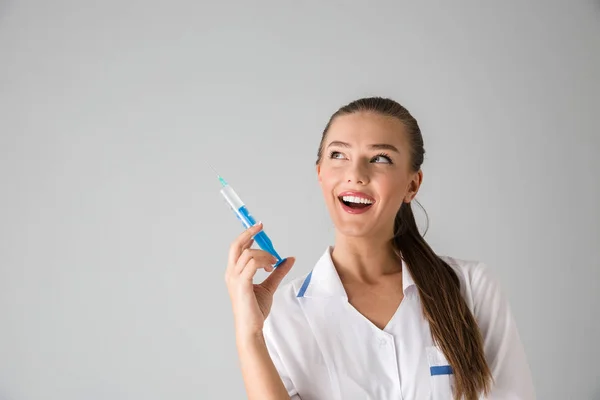 Schöne junge Frau Kosmetikerin Arzt isoliert über graue Wand Hintergrund hält Injektionsspritze. — Stockfoto