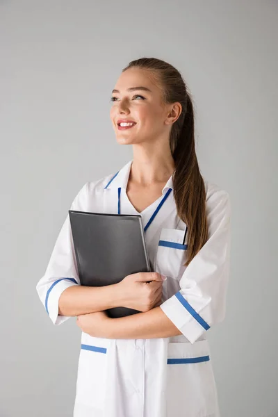 Bela feliz jovem cosmetologista médico isolado sobre cinzento parede fundo segurando pasta . — Fotografia de Stock