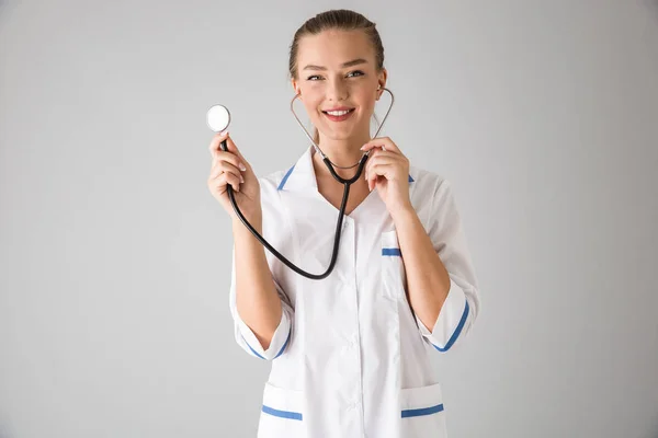 Kosmetologe Arzt isoliert über graue Wand Hintergrund hält Stethoskop. — Stockfoto