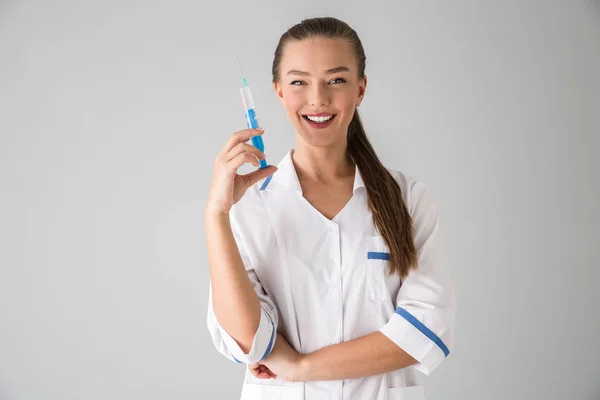 Beautiful young woman cosmetologist doctor isolated over grey wall background holding injection syringe. — Stock Photo, Image