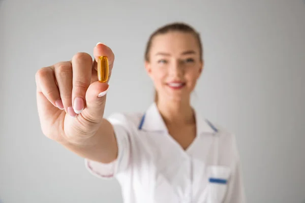 Beautiful young woman cosmetologist doctor isolated over grey wall background holding pill vitamin. — Stock Photo, Image