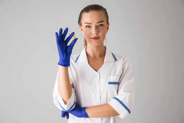 Mooie jonge vrouw schoonheidsspecialist arts geïsoleerd over grijs muur achtergrond houden vitamine pil. — Stockfoto