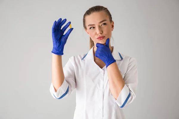 Bella giovane donna cosmetologo medico isolato su sfondo grigio parete contenente vitamina pillola . — Foto Stock