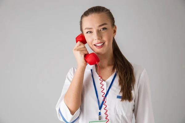 Bonita jovem cosmetologista médico isolado sobre fundo de parede cinza falando por telefone . — Fotografia de Stock