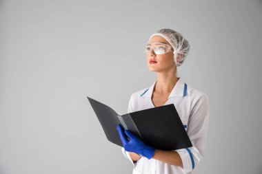 Güzel genç kadın Güzellik Uzmanı Doktor klasör tutan gri duvar arka plan üzerinde izole.