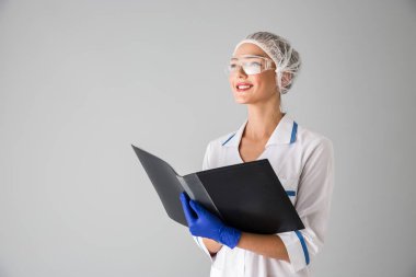 Güzel genç kadın Güzellik Uzmanı Doktor klasör tutan gri duvar arka plan üzerinde izole.