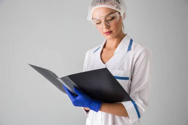 Güzel genç kadın Güzellik Uzmanı Doktor klasör tutan gri duvar arka plan üzerinde izole.