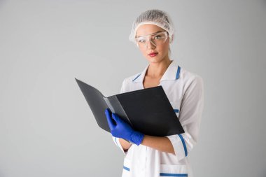 Güzel genç kadın Güzellik Uzmanı Doktor klasör tutan gri duvar arka plan üzerinde izole.