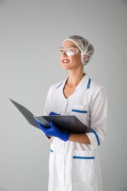Güzel genç kadın Güzellik Uzmanı Doktor klasör tutan gri duvar arka plan üzerinde izole.