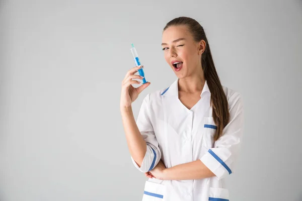 注射器を保持している灰色の壁背景に分離された美しい若い女性美容師医師. — ストック写真