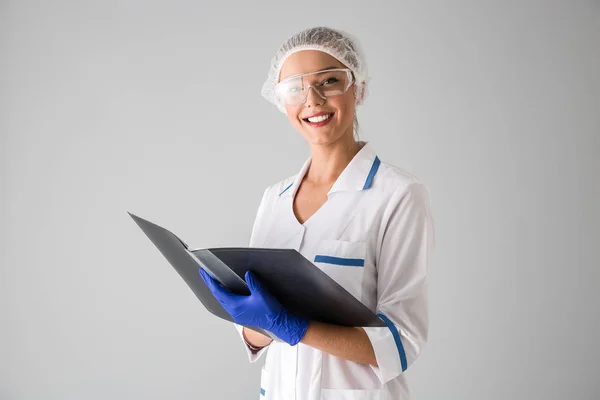 Schöne junge Frau Kosmetikerin Arzt isoliert über graue Wand Hintergrund hält Ordner. — Stockfoto