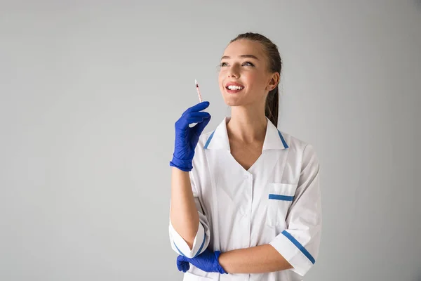 注射器を保持している灰色の壁背景に分離された若い女性美容師医師. — ストック写真