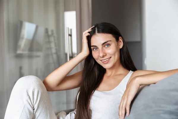 Glada vacker ung kvinna som sitter på soffa inomhus hemma. — Stockfoto