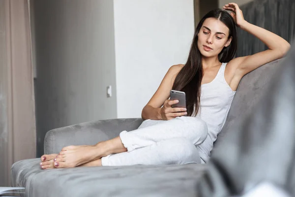 Красивая молодая женщина сидит дома на диване и разговаривает по мобильному телефону. . — стоковое фото