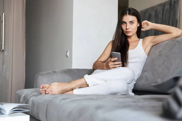 Nagyon szép fiatal nő ül a kanapén beltéri otthon használ mozgatható telefon beszélgetés. — Stock Fotó