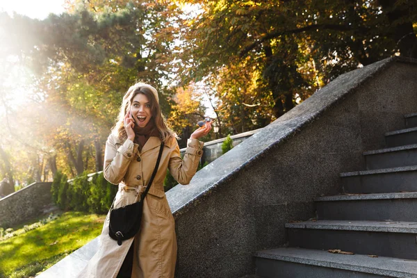 Aufgeregter schockierter junger schöner Frau im Straßenpark, die mit dem Handy spricht. — Stockfoto