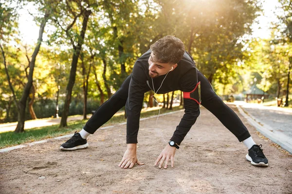 Handsome young sports fitness man runner outdoors in park make exercises. — Stock Photo, Image