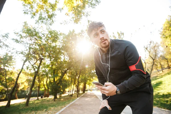 Przystojny młody Sport fitness mężczyzna runner na świeżym powietrzu w parku słuchania muzyki za pomocą słuchawek. — Zdjęcie stockowe